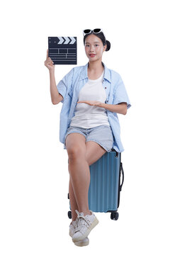 Woman with Clapperboard: A cheerful woman sits atop a travel suitcase, holding a clapperboard. She radiates positivity, suggesting an upcoming adventure or creative project.
