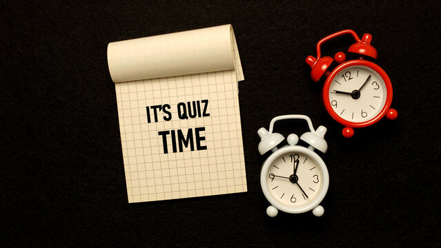It's Quiz Time motivational text on notepad with red and white mini alarm clocks on black background