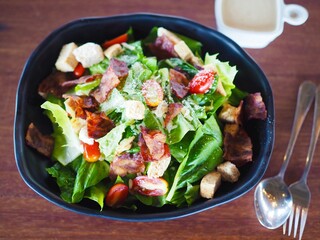 A salad with bacon sits in a balck bowl on the dining table.