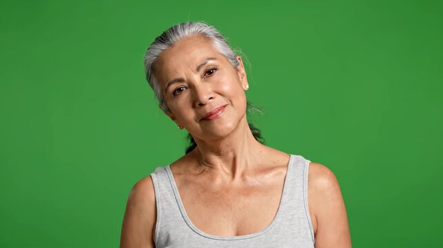 Active older woman stretching arms behind head against vibrant green screen