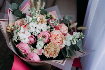 Soft natural light bouquet of pastel roses, carnations and white flowers with eucalyptus in elegant wrapping, close-up romantic still life without people