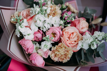 Soft natural light bouquet of pastel roses, carnations and white flowers with eucalyptus in elegant wrapping, close-up romantic still life without people