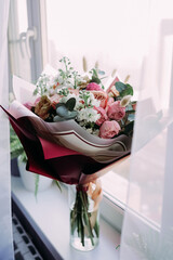 Soft airy light bouquet of pastel roses and white flowers in elegant wrapping on a windowsill, glass vase with eucalyptus and sheer curtains, romantic indoor still life without people