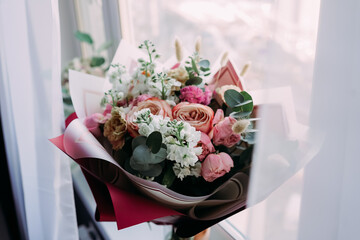 Soft natural light bouquet of pastel roses and white flowers by a window, elegant wrapping with eucalyptus leaves, romantic spring still life without people