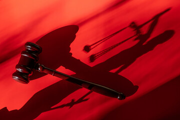A conceptual story about correction in the judicial system with a judge's gavel and a long shadow from the figure of Themis on a red background.
