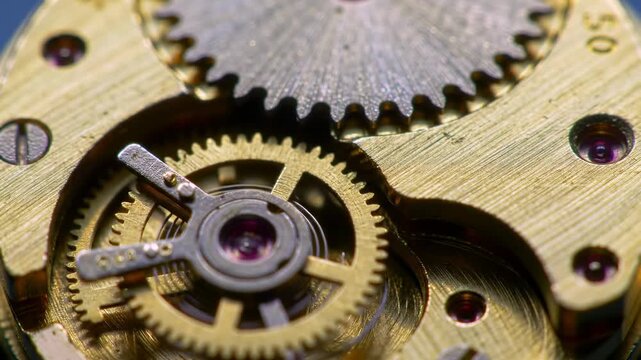 A close-up view shows the intricate mechanics of a tiny device. Gears of varied sizes and delicate parts form a golden mechanism