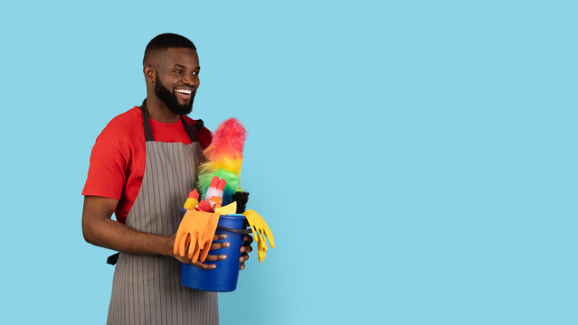 Cleaning Offer. Excited Black Male Cleaner Holding Basket With Detergents And Looking Aside At Copy Space Over Blue Background, Cheerful African American Man Ready For Spring Cleaning, Panorama