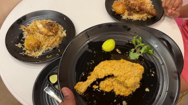 Spicy chicken chap served with biryani and mutton stew in black plate in Kolkata