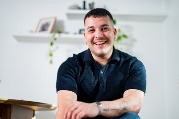 A cheerful man in his 30s relaxes indoors, exuding a friendly vibe