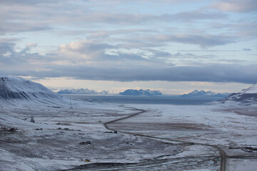 Longyerbeyen, Svalbard, Snowy landscape with a road running through it. The sky is cloudy and the sun is setting