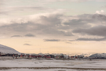 Longyerbeyen, Svalbard, Snowy landscape with a small town in the distance. The sky is cloudy and the sun is setting