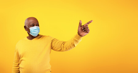 Elderly black man wearing a surgical face mask gestures toward a blank area, inviting text or ads. The bright orange background creates a warm and inviting atmosphere during the pandemic.