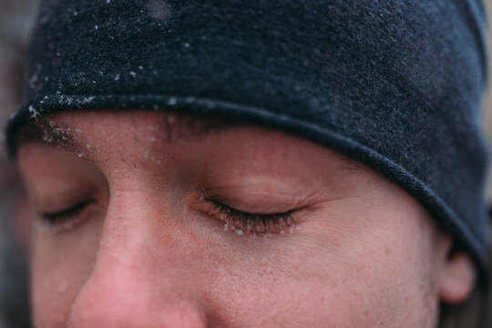 Close-up of a man’s closed eyes in a winter beanie with delicate snowflakes on lashes, soft natural light and shallow depth of field for a calm cold weather mood