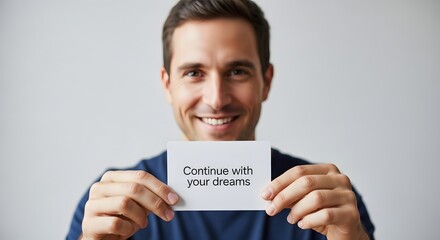 A smiling man holding a card with the message 'Continue with your dreams' in a well-lit, professional setting, inspiring motivation and positivity