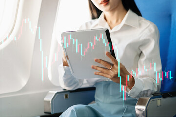 Asian businesswoman analyzing stock market data on tablet during airplane flight. Concept of finance, investment, fintech, and digital economy.