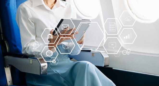 Asian businesswoman using tablet with digital interface icons during airplane flight. Concept of technology, innovation, and smart business travel.