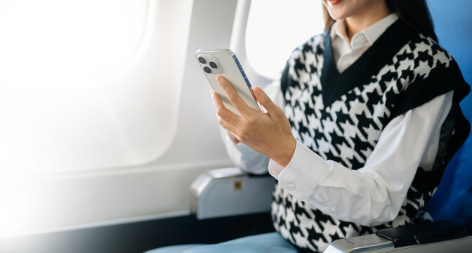 Asian businesswoman using tablet with stylus during airplane flight. Concept of business travel, digital lifestyle, and remote work flexibility.