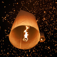 hundreds of paper lanterns glowing in the night sky during yi peng festival in chiang mai, thailand, as warm flames lift them gently, symbolizing wishes and letting go.