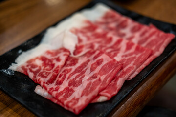 A close-up shot of sliced raw meat, arranged on a plate, ready to be cooked in a hot pot