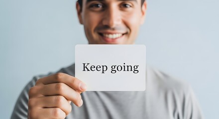 A smiling man holding a sign with the motivational message 'Keep going' in a bright and positive setting