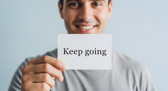 A smiling man holding a sign with the motivational message 'Keep going' in a bright and positive setting - Powered by Adobe