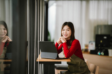 A smiling barista in a red sweater and apron holds a tablet while standing inside a cozy coffee shop.