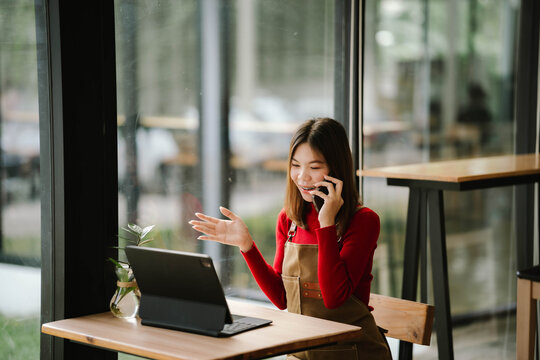 A woman sitting in a cafe working on a tablet while checking her smartphone, with coffee and a small plant on the table.