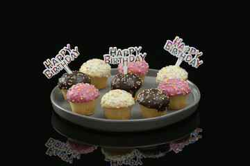 Colourful birthday Cupcakes on a plate sitting on a black reflective surface