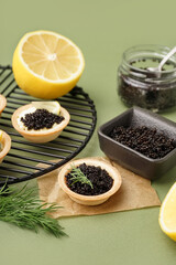 Grid of tasty tartlets with black caviar on green background