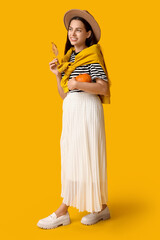 Stylish young woman with fresh pumpkin and autumn leaf on yellow background