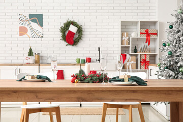 Christmas table setting with burning candles and wreath in kitchen