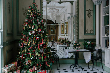 Elegant living room interior decorated for Christmas with a large decorated tree, a pile of presents, and a tiled black and white floor