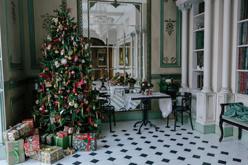Elegant living room interior decorated for Christmas with a large decorated tree, a pile of...