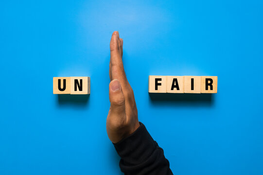 male hand put away first two letter from unfair word to be read fair isolated on blue background. fairness concept