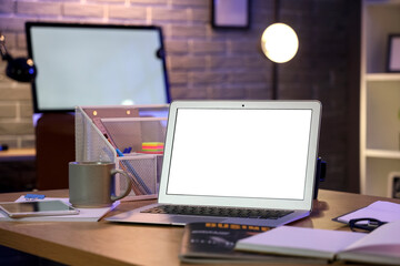 Blank laptop with stationery on desk in office at night, closeup