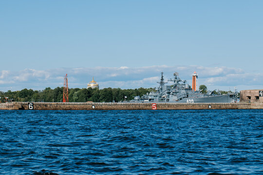 Historic Fort 2 structure with the Russian Navy flag waving and a large grey warship moored behind it on a bright summer day in Kronstadt - Powered by Adobe
