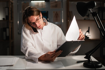 Young male doctor making a phone call working during night shift in hospital office