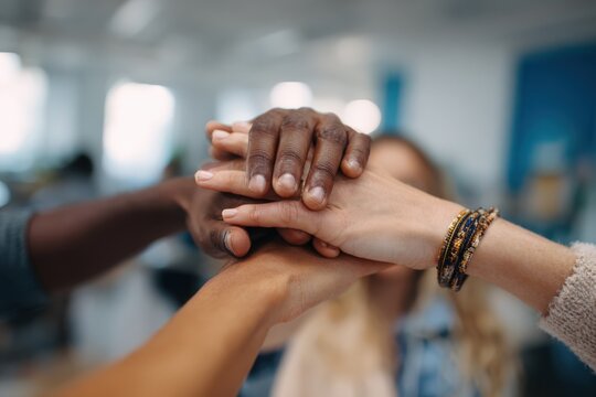 Diverse group of hands coming together in a collaborative gesture, symbolizing teamwork and unity in a bright office environment, showcasing solidarity and support among individuals