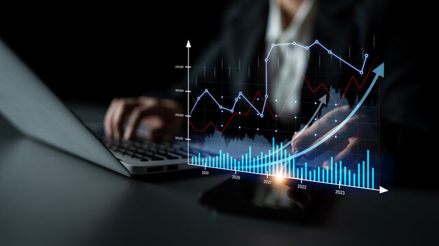 A business professional engaged in analyzing digital financial data on a laptop. The image features graphs and charts symbolizing growth and technology in a dark setting. Scalp