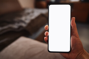 Man hold smartphone with white screen in his hand sitting on a couch in home environment