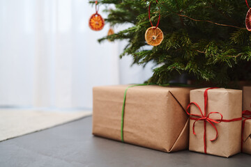 Small christmas tree with gifts in paper wrap near window