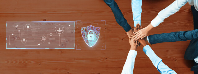A diverse team of hands forms a united stack as they focus on digital security. An overlay of technology graphics and a lock icon symbolizes protection and collaboration in a modern workspace. Trope