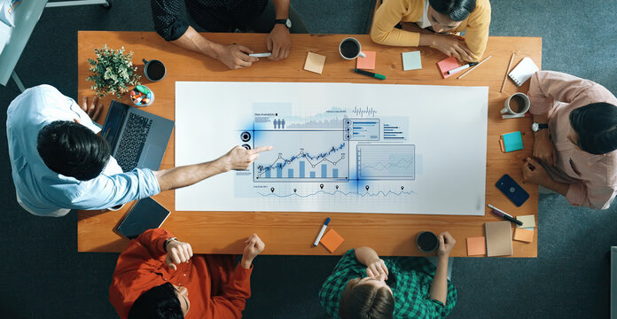 Group of professionals engaged in a business meeting focusing on analytics and strategy, showcasing collaboration in a modern office environment with digital tools. Trope - Powered by Adobe