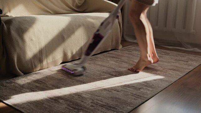 Barefoot woman dancing vacuums the carpet in the living room. The legs of a cheerful housewife while cleaning the room. - Powered by Adobe