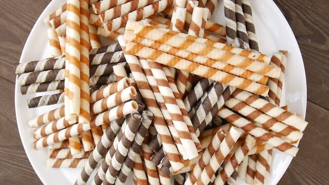Delicious assorted chocolate and vanilla striped wafer rolls rotating on a white plate.