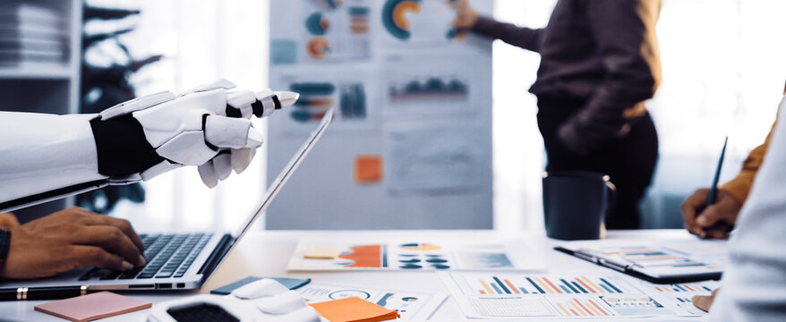 A modern office scene showcasing a robot assistant collaborating with a human team in a business meeting. Team members analyze data presented on charts and graphs.Noogenesis
