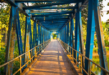 Blue metal Sadolxem bridge surrounded by tropical greenery at golden sunset in South Goa, India
