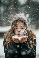 Girl Blowing Snow in Winter Wonderland Outside While Wearing Beanie and Cozy Coat