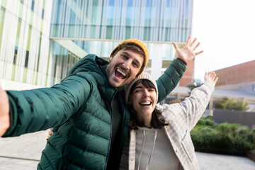 Happy couple taking selfie while walking in city center during winter vacation