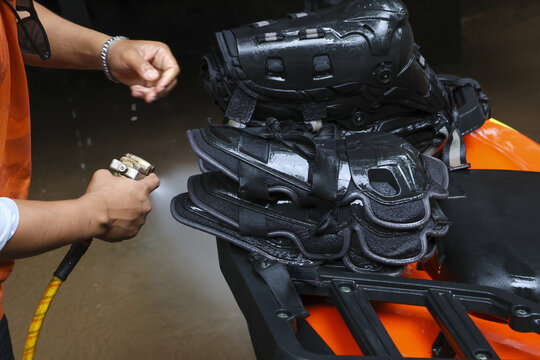Focused man diligently washing black protective knee brace gear with high pressure water spray hose after an extreme sport activity, getting ready for next ride